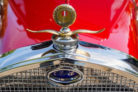 Winged radiator mascot and Ford badge on a red vintage car at a classic car meet