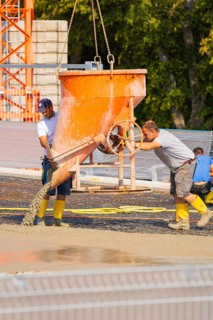 A concrete container empties its contents onto a construction site, checked by two workers,