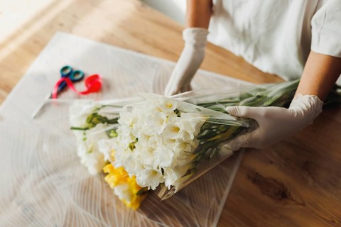 A person in gloves carefully arranges white and yellow flowers on a wooden table during a floral