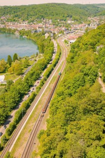 Aerial view of a city with river and railway lines, surrounded by lush forests, construction site