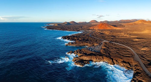 Coast with lava fields, volcanic landscape near Los Hervideros with red volcano Montaña Bermeja, in