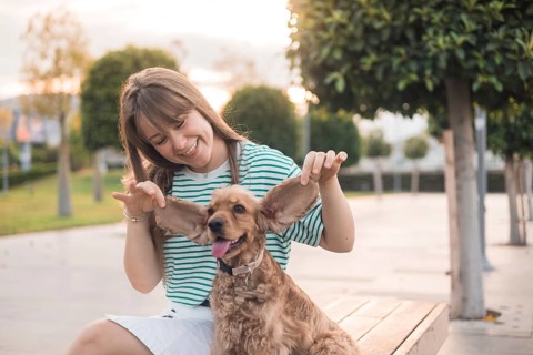 A woman joyfully interacts with her dog in a sunny park setting