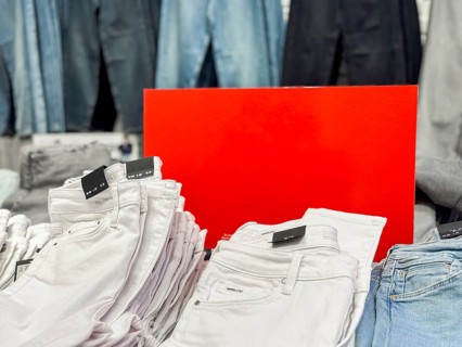 A display of folded white jeans in a retail store. Behind them, various shades of blue denim pants