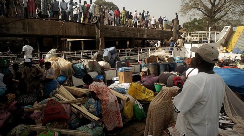 A ship is being loaded, people in traditional clothing and goods crowd on the deck of an old ferry