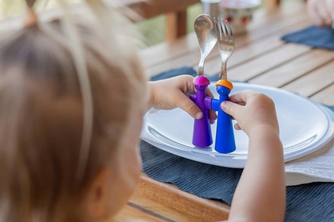 Young child interacts with colorful utensils, engaging in imaginative play at a wooden table during