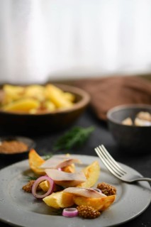 Plate contains potato wedges and herring garnished with onion. Mustard placed around dish.