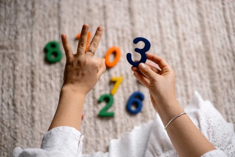 Hands counting with a blue number three over a scattered number arrangement