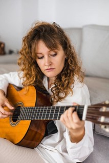 Curly-haired woman focused on playing the guitar in a white shirt