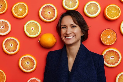 Smiling young woman in dark blue coat with citrus background