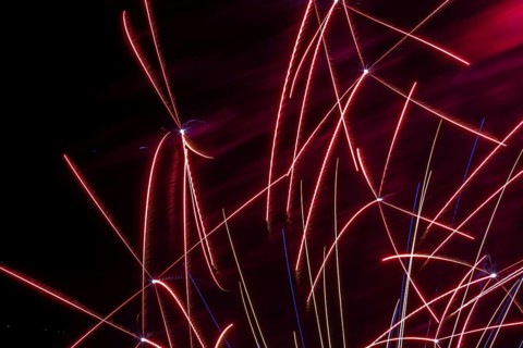 Red, white and blue illuminated trailing streaks of fireworks in black sky at night in summer,