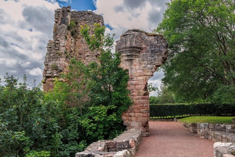 The ruined towers of 14th-century Rosslyn Castle stand beside a gravel path under blue sky in