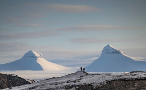 Two people, including a photographer with a stand in front of two of the three mountains Tee