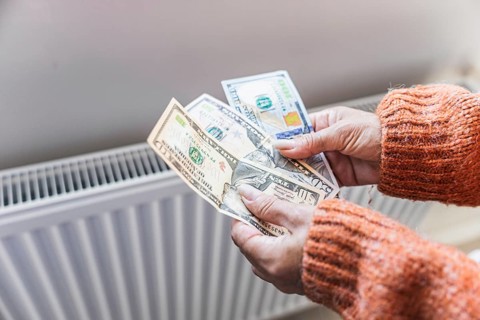 Winter home heating expenses and rising utility costs. Woman counting US dollar cash near radiator