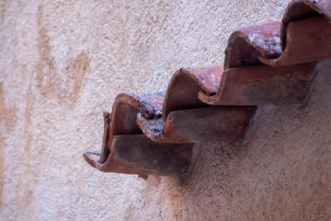 Curved terracotta roof tiles project from a textured pale wall as a small architectural detail,