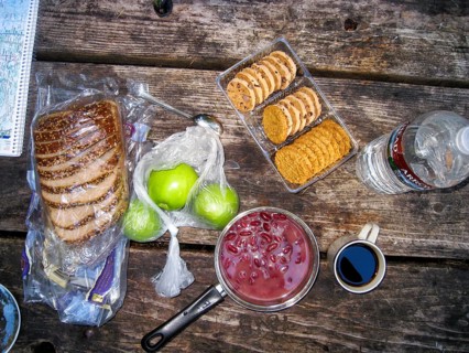 View from above of a rustic camping table with bread, apples, cookies, kidney beans in a cooking