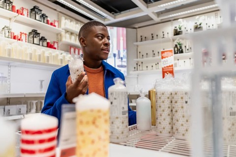 A person explores a store that sells candles, holding one candle while looking at many other