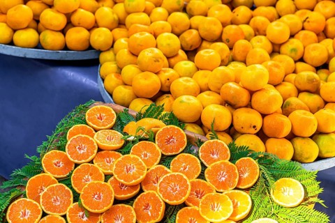 Fresh oranges and mandarins displayed at a market. Whole oranges are piled high, while sliced