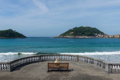 Woman sitting on a bench on the promenade at Bicentennial Balcony, La Concha beach, San Sebastián,
