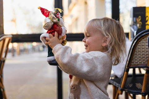 A young Caucasian girl with blonde hair smiles while holding a Santa Claus figurine. The scene is