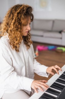 A woman in a white shirt plays the piano in a casual living room setting