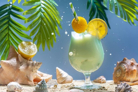 Sparkling cocktail with lemon and straw surrounded by mussels and palm leaves