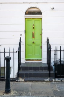 Light green front door with gold fittings in white house facade surrounded by black metal railing,