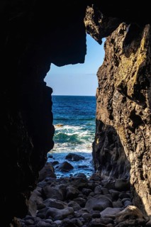 Dark lava rock cave revealing the dramatic blue atlantic ocean with white waves crashing upon the