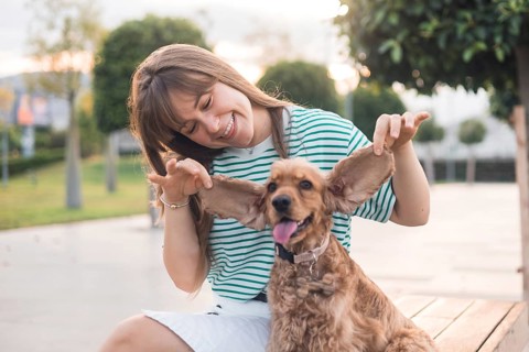 A woman playfully laughs with her dog, both sitting on a park bench