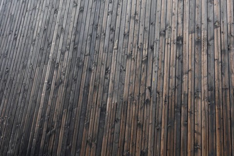 Close-up of a textured wooden surface with dark brown and black tones. The wood has a natural grain