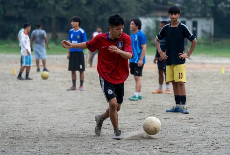 Children play football on a dusty neighbourhood field, chasing the ball with energy and