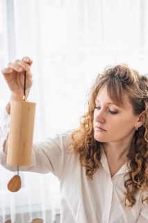 A focused woman in a white shirt carefully holding a wooden chime