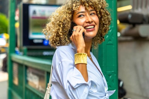 Young woman with curly hair talking on a mobile phone, laughing and enjoying urban life near a