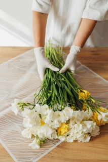 A person in gloves carefully arranges a bunch of fresh flowers, combining vibrant yellow and white