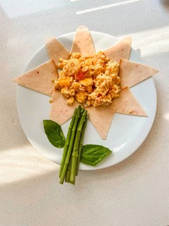 A creative children breakfast plate arranged like a flower. Scrambled eggs in the center,