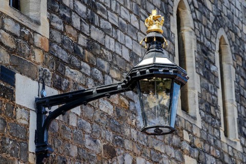 A black iron lantern topped with a gilded crown projects from a stone wall within Windsor Castle,