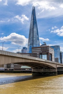 The shallow arch of London Bridge crosses the River Thames beneath the soaring glass facets of The