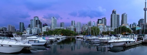 Yachts and sailboats moored at a harbour marina with high rise skyline buildings and skyscrapers