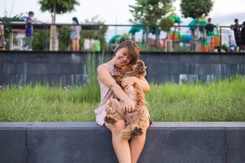 Woman embraces her dog joyfully, with a playground and greenery in the background