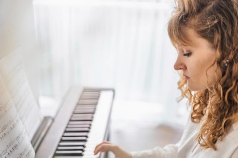 A woman with curly hair plays the piano, focused on the sheet music in a softly lit room