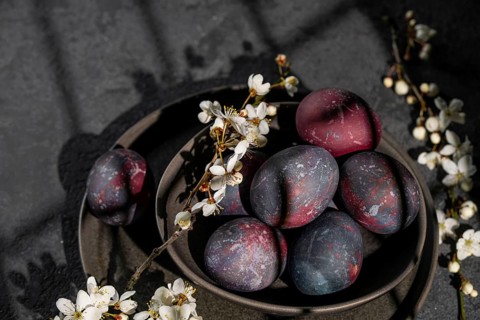 From above, a rustic bowl filled with galaxy-inspired Easter eggs sits amid delicate white flowers