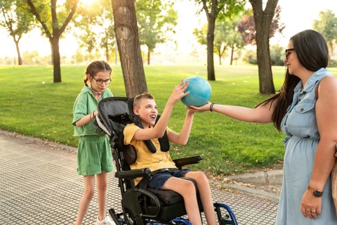 A warm family moment in a park, with a girl using a tracheostomy and a boy with cerebral palsy