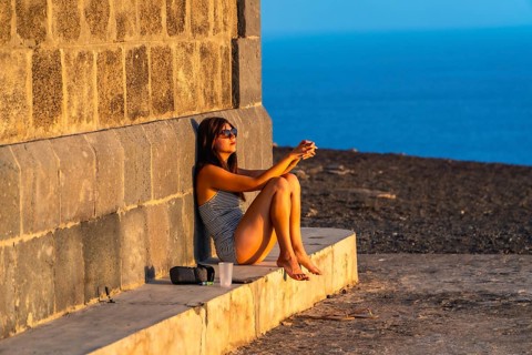 Woman resting against a stone wall, enjoying the warm light of the setting sun overlooking the