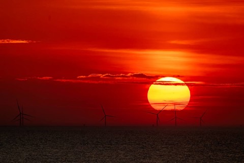 Dramatic sunset over the sea, wind turbines and wind turbines on the horizon, streaks of clouds,