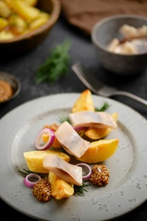 Dish features potato wedges and herring arranged on plate with mustard and sliced onion. This meal