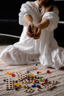 Person in white dress kneeling with scattered wooden toys and colorful balls