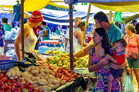 Mother holds child at a lively market with lots of fruit and vegetable stands, market scene in a