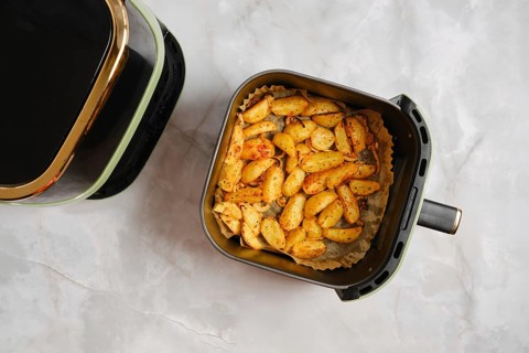 Top view of golden roasted potato wedges cooked in air fryer with spices. Basket sits on marble