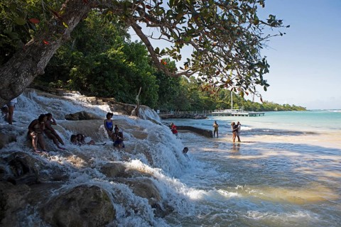 Jamaican woman sit on rocks at Dunn's River Falls or waterfalls at the mouth of the Caribbean Sea,