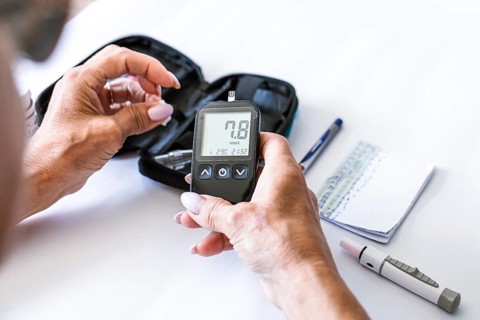 Woman inserting a test strip into a blood glucose meter before measuring blood sugar at home.