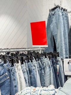 A display of various denim jeans hanging on a rack in a clothing store. A bright red sign is